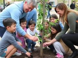 Families and children planting a tree together in a public space, symbolizing community engagement and generational knowledge sharing.